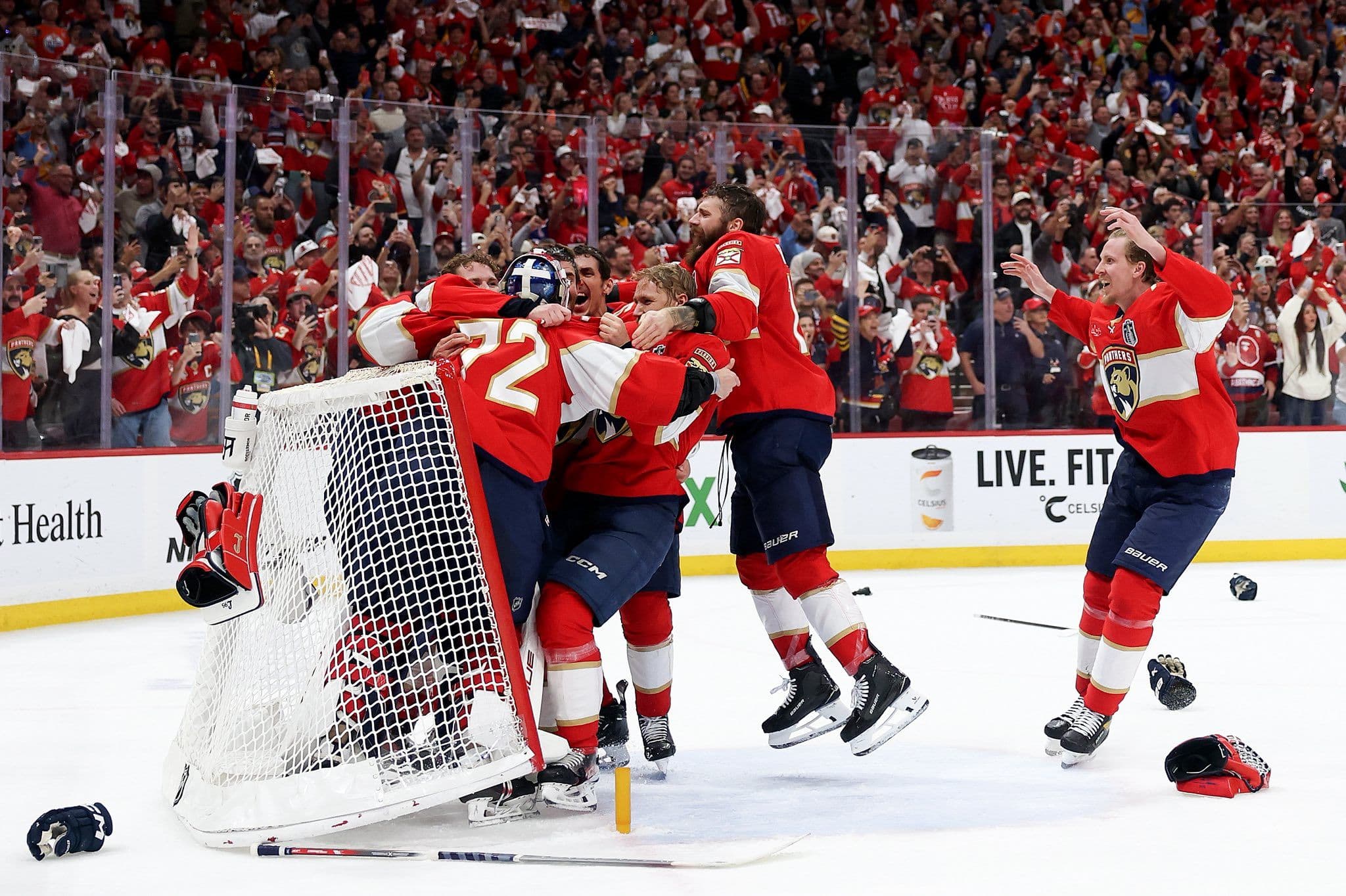 Florida Panthers hockey players celebrate on the ice near the goal as fans cheer in the stands, with discarded gloves and sticks scattered on the rink