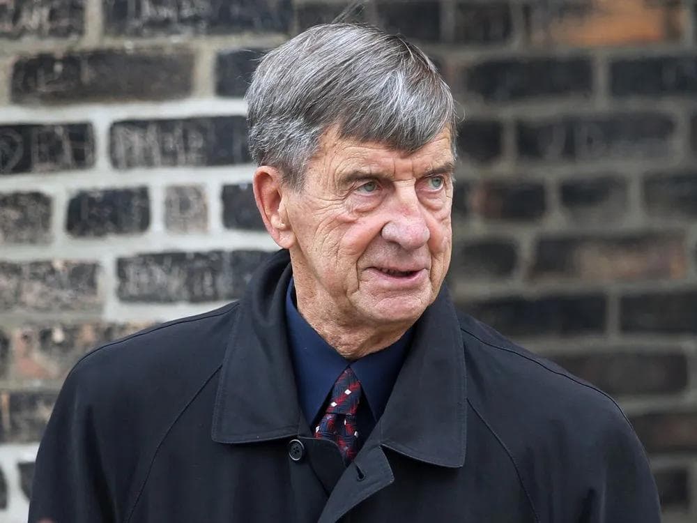 Ted Lindsay in his later years, wearing a dark coat in front of a brick wall.